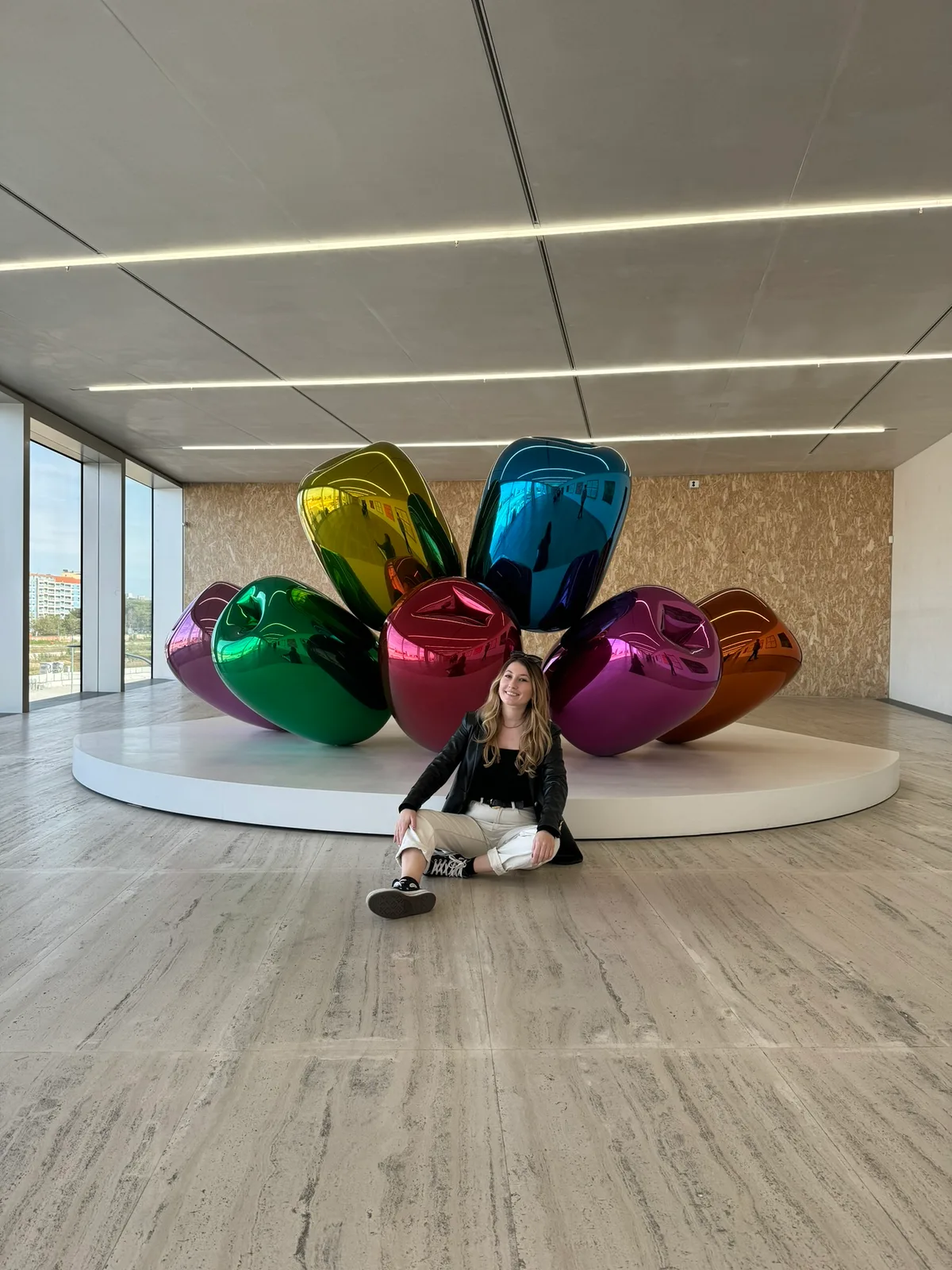 Milijana sitting on the floor in front of a sculpture of giant colourful metallic balloons